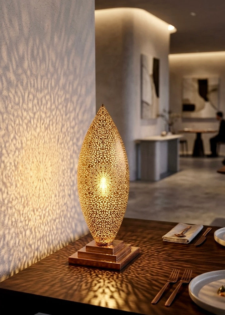 An elegant Moroccan brass table lamp illuminated on a dark wooden restaurant table, casting intricate shadow patterns on the wall in a luxury dining room.⁠