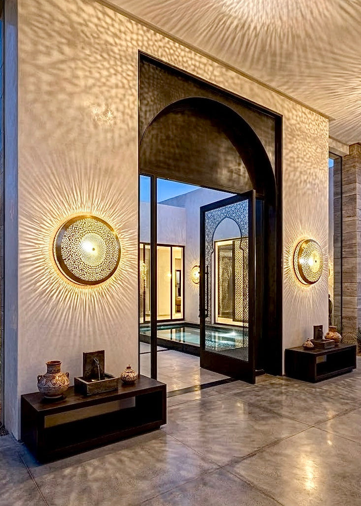 Pair of illuminated handmade Moroccan brass wall sconces flanking a grand arched entrance in a modern luxury villa.