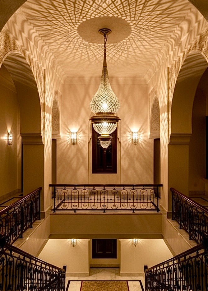 Grand Moroccan brass ceiling lamp creating intricate shadow patterns in a luxury staircase hallway.