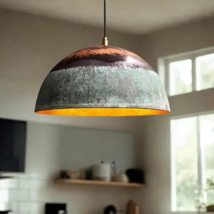 Minimalist aged copper dome pendant light with warm interior glow and patina finish.