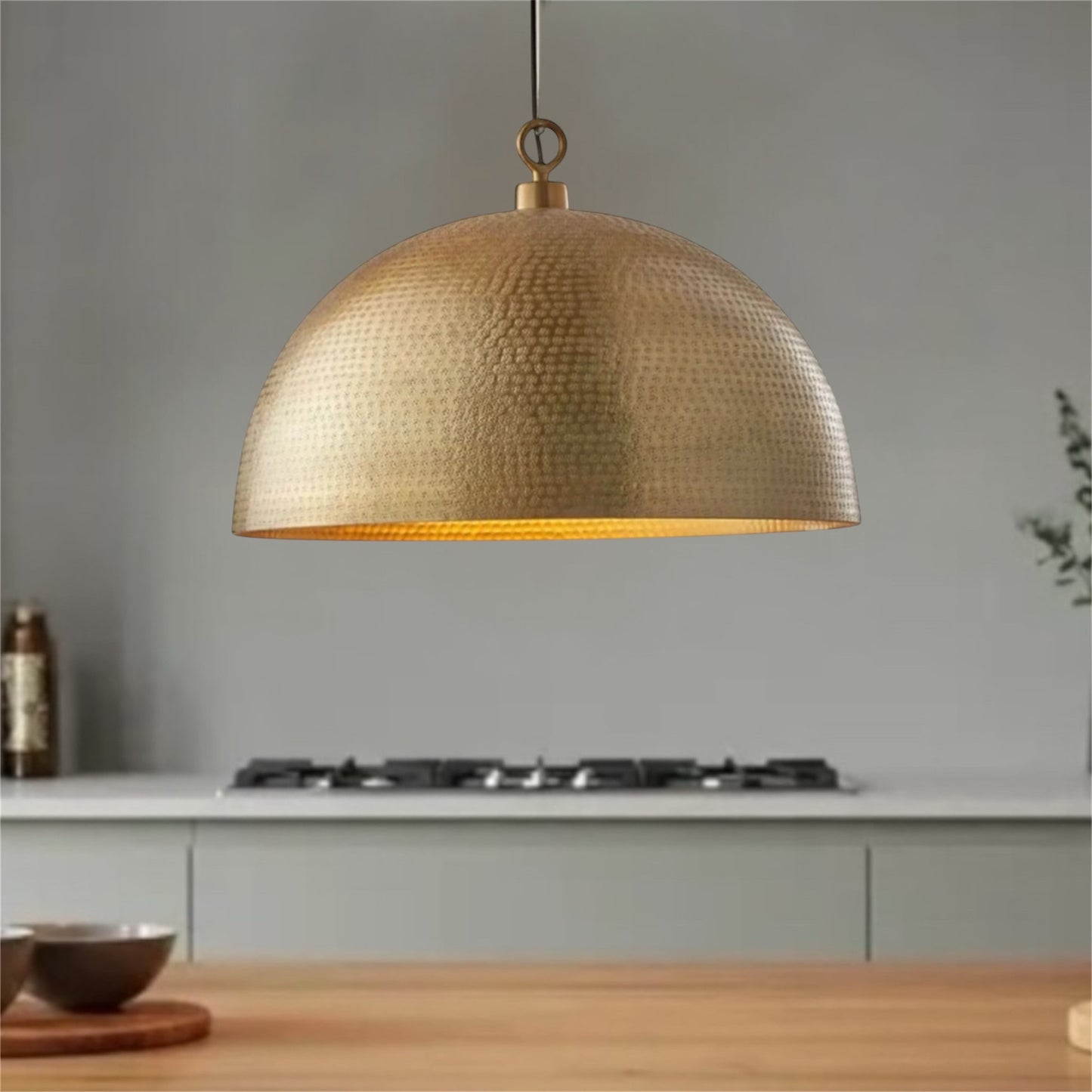 Single modern dome pendant light in hammered brass hanging over a kitchen stove.