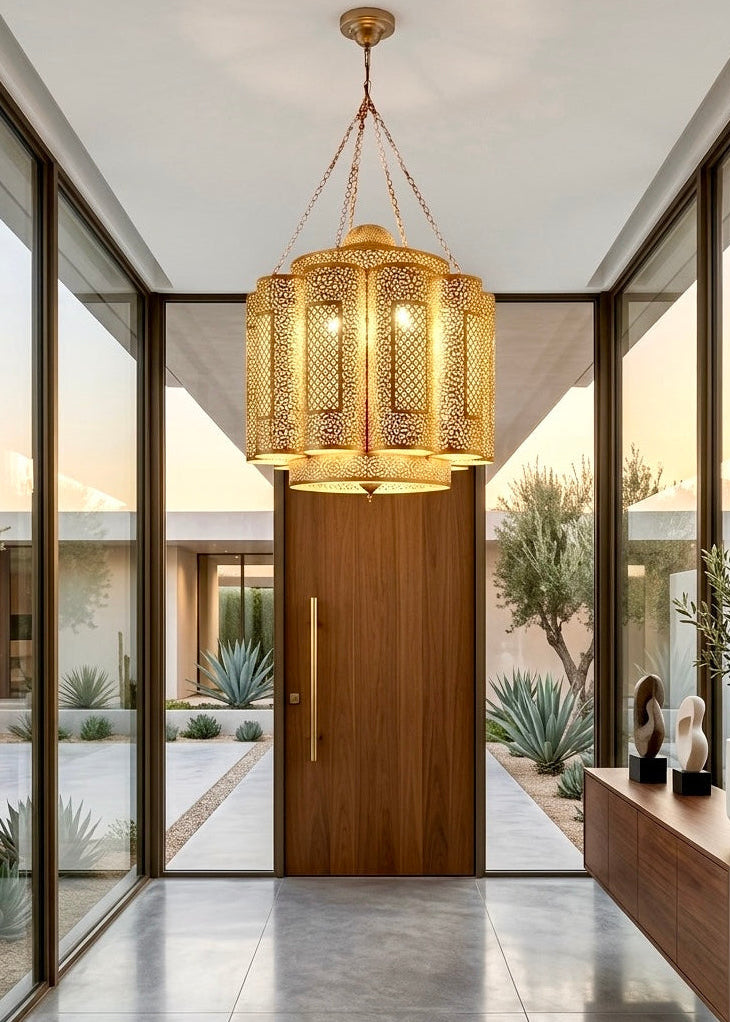 Handcrafted modern Moroccan brass chandelier hanging in a minimalist luxury villa entryway with floor-to-ceiling glass windows and desert view.