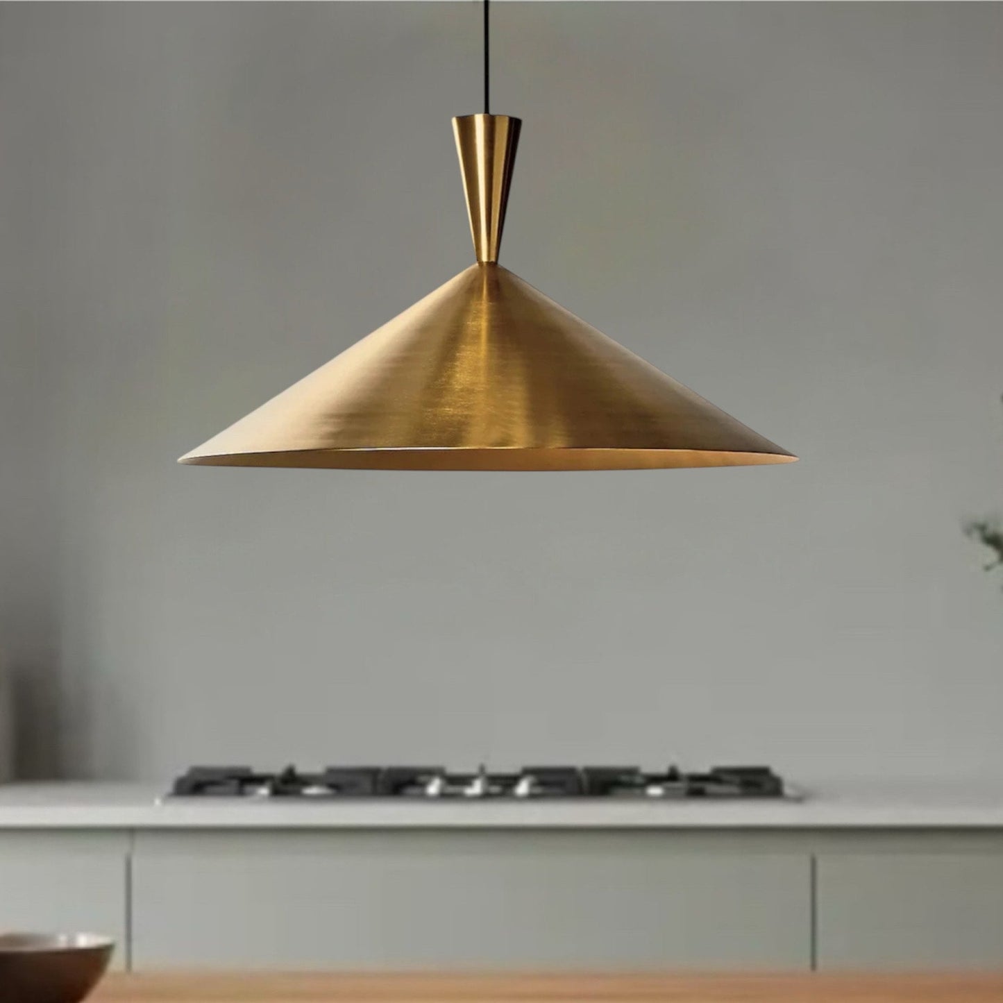 Close-up of a modern gold cone-shaped pendant light with a brushed brass finish, minimalist ceiling lamp for contemporary interiors.