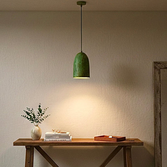Modern handmade brass pendant lamp with green patina hanging over a wooden console table in a minimalist entryway.