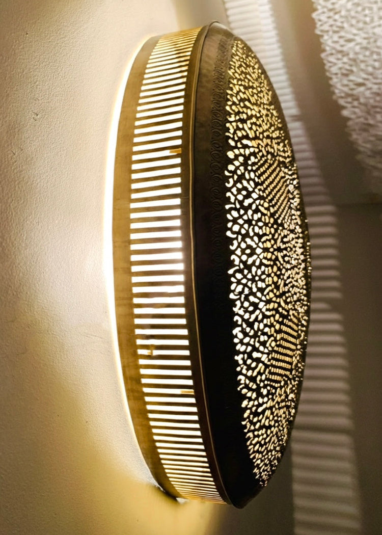 Side view of a modern Moroccan brass wall lamp with a warm glow, showcasing the slotted brass frame and the golden finish of the metalwork