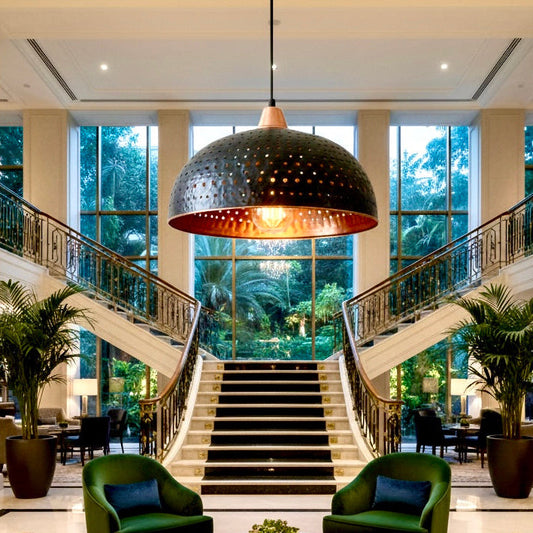 Large handmade black and brass hammered dome pendant light hanging in a luxury hotel lobby with a grand staircase.