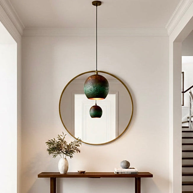 Elegant verdigris copper lamp reflecting in a round mirror above a wooden console table in a minimalist hallway.