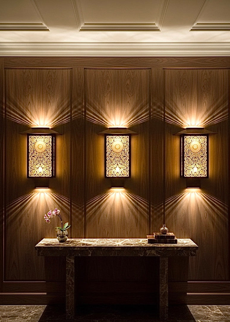 Set of three hand-etched Moroccan brass wall sconces on a dark wood panel for office decor.