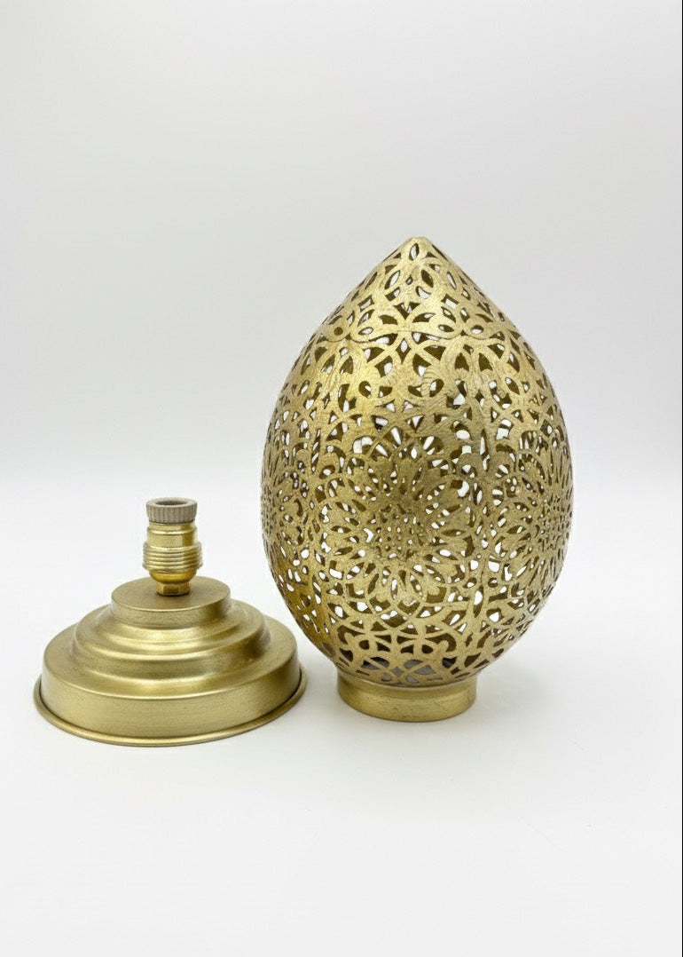 A glowing Moroccan table lamp placed on a traditional bone inlay side table in a dark bedroom with a city view.