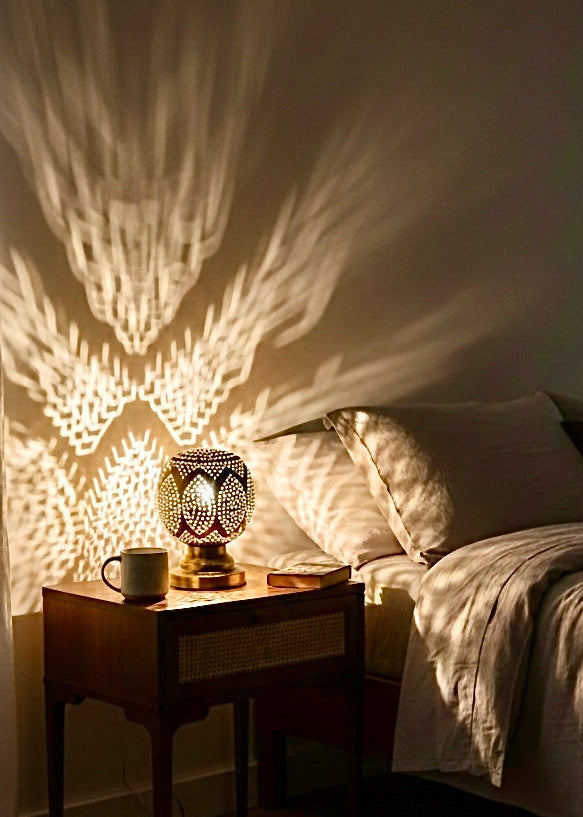 Antique brass Moroccan lamp used as a bedside light on a wooden nightstand, enhancing the bedroom decor with soft, patterned lighting.