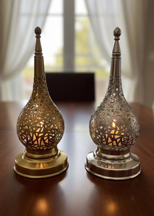 Pair of Moroccan brass candle lamps in gold and silver finishes on a wooden table.background