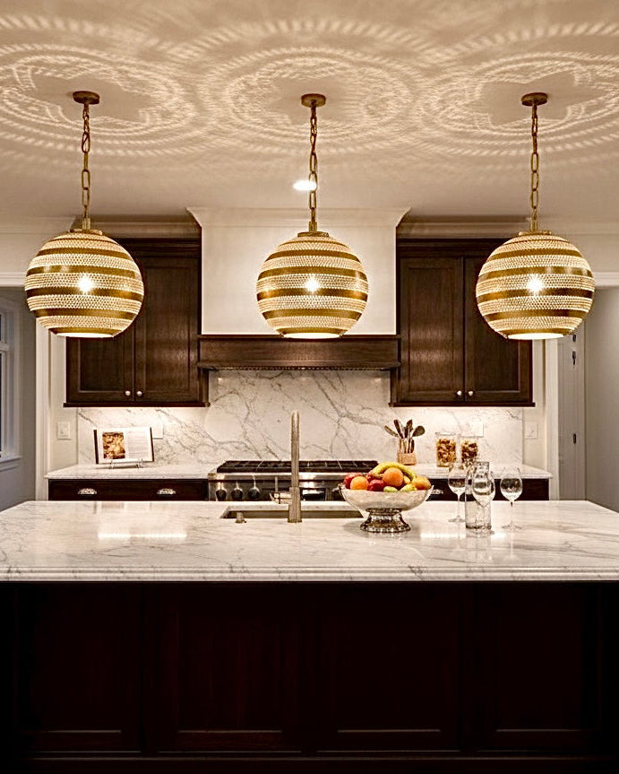 Three Moroccan brass hanging lamps installed over a white marble kitchen island in a modern dark-wood kitchen.