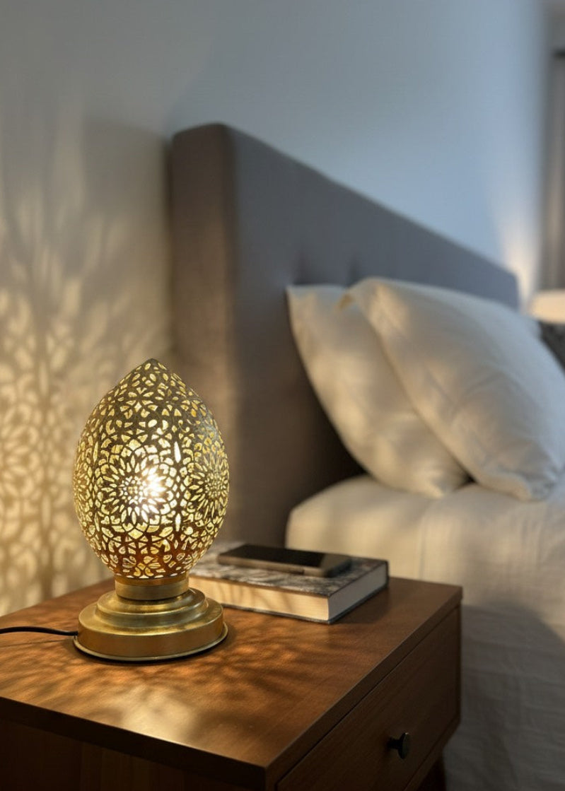 A close-up of an egg-shaped Moroccan table lamp made of gold brass with intricate geometric floral perforations.