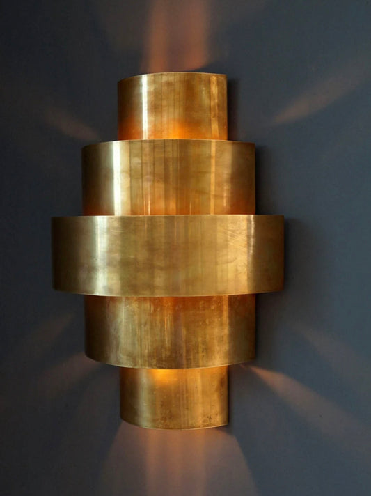 Handmade Moroccan brass wall lamp with 3-tier cylindrical design glowing on a textured wall.
