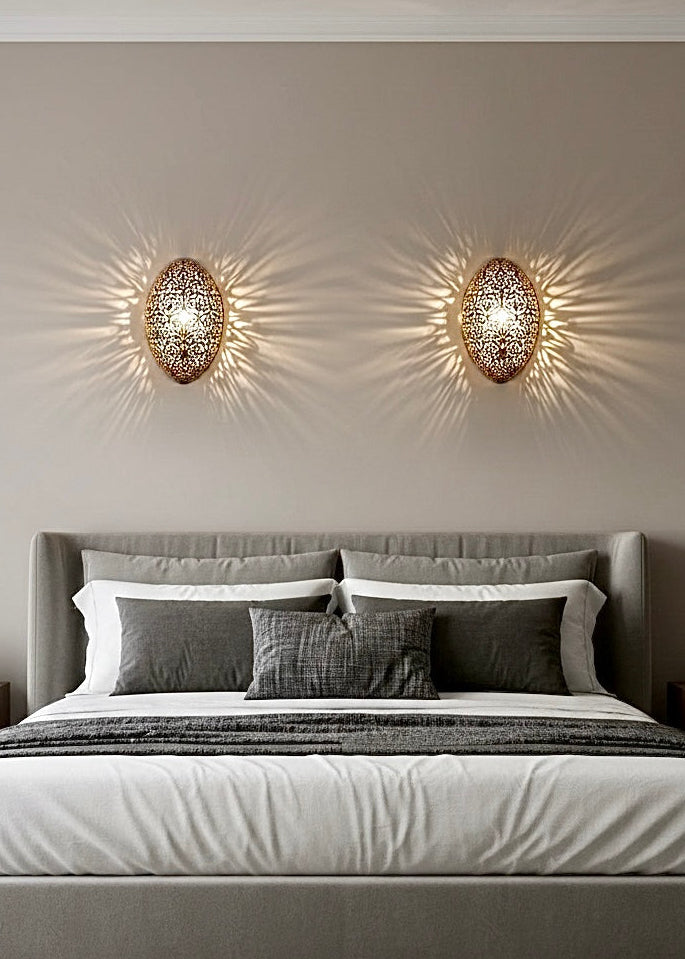 Handmade Moroccan brass wall sconce installed in a cozy bedroom, casting warm geometric light patterns on the wall.