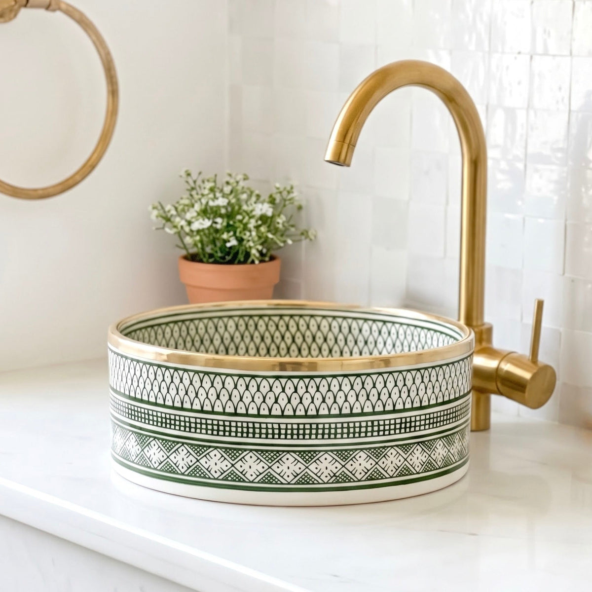 Green and white handmade Moroccan ceramic vessel sink with brass rim edge placed on white marble vanity top next to brass faucet