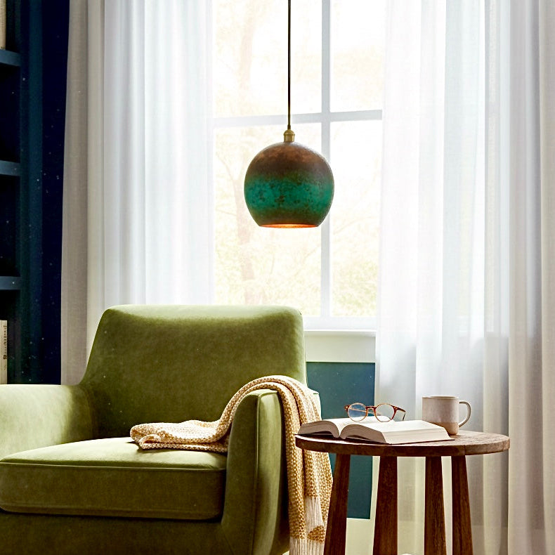 Handcrafted green patina copper pendant light hanging over a green velvet armchair in a cozy reading corner.