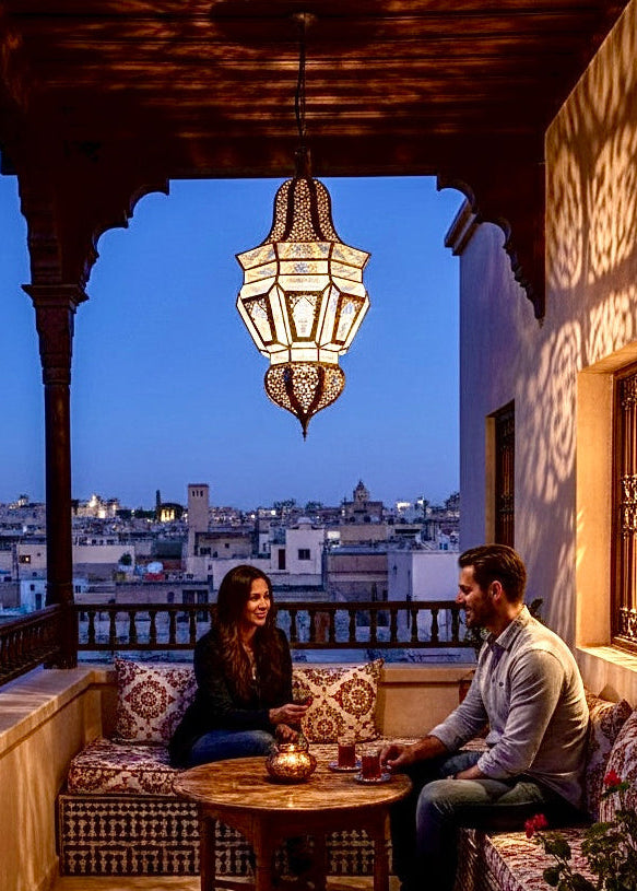 Traditional Moroccan brass lamp lighting up an outdoor terrace at night with a view of the city.