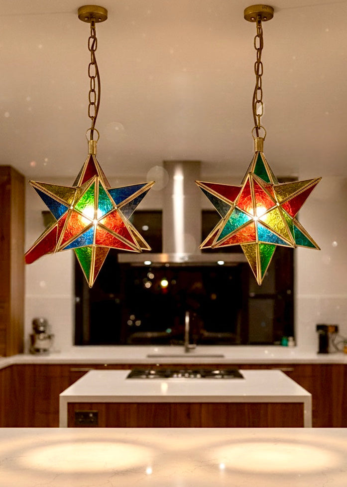 Two handmade Moroccan star pendant lights with multicolored glass panels and brass frames hanging over a modern white kitchen island.