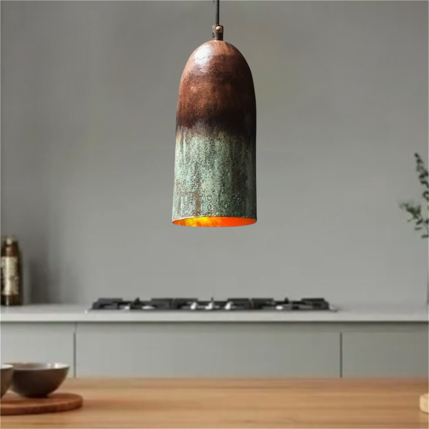 Close-up of a rustic copper pendant light with a natural green patina and warm orange interior glow.