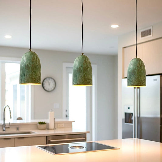 Trio of artisan handmade brass pendant lights with verdigris finish installed over a modern white kitchen island.
