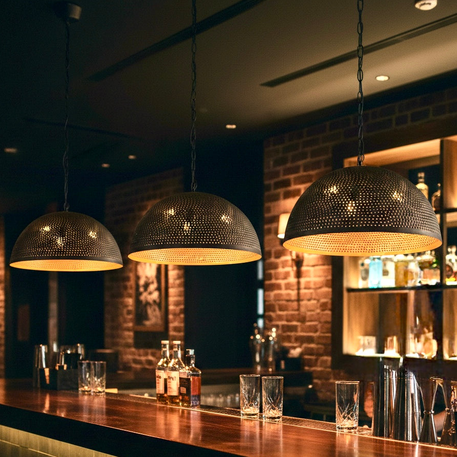 Set of three perforated black brass dome lights with warm gold glow over a luxury bar counter.