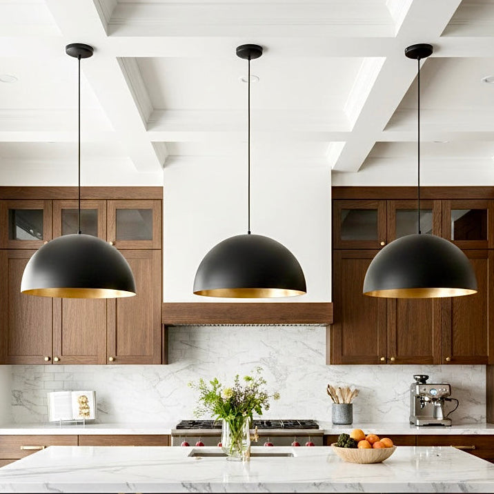 A trio of modern black dome pendant lamps with warm gold interiors installed over a wooden kitchen bar with blue stools.