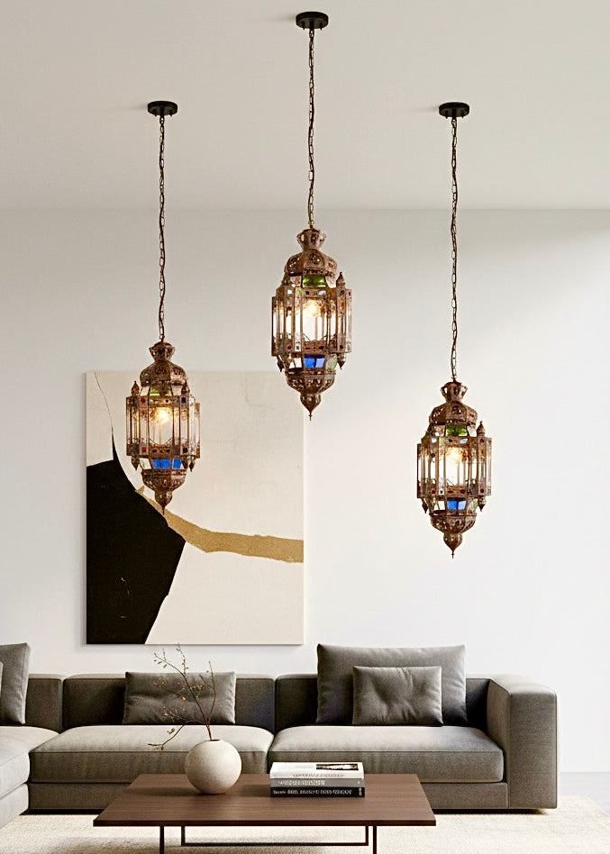 Set of three colorful Moroccan glass pendant lights hanging at different heights over a modern grey sofa and coffee table.