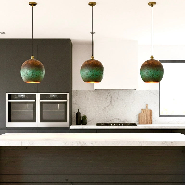 Three rustic Moroccan-style pendant lights with green oxidation hanging over a contemporary marble kitchen island.
