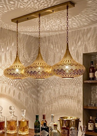 Three artisanal brass pendant lights installed over a modern bar counter, creating a warm ambiance.