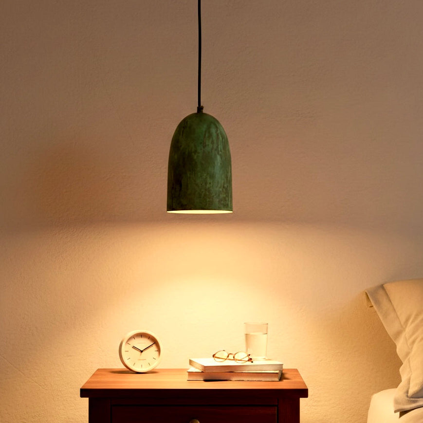 Vintage style brass hanging lamp with green patina providing warm light over a wooden nightstand in a cozy bedroom.