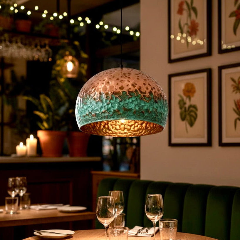 Artisan copper pendant light illuminating a wooden dining table in a cozy restaurant.