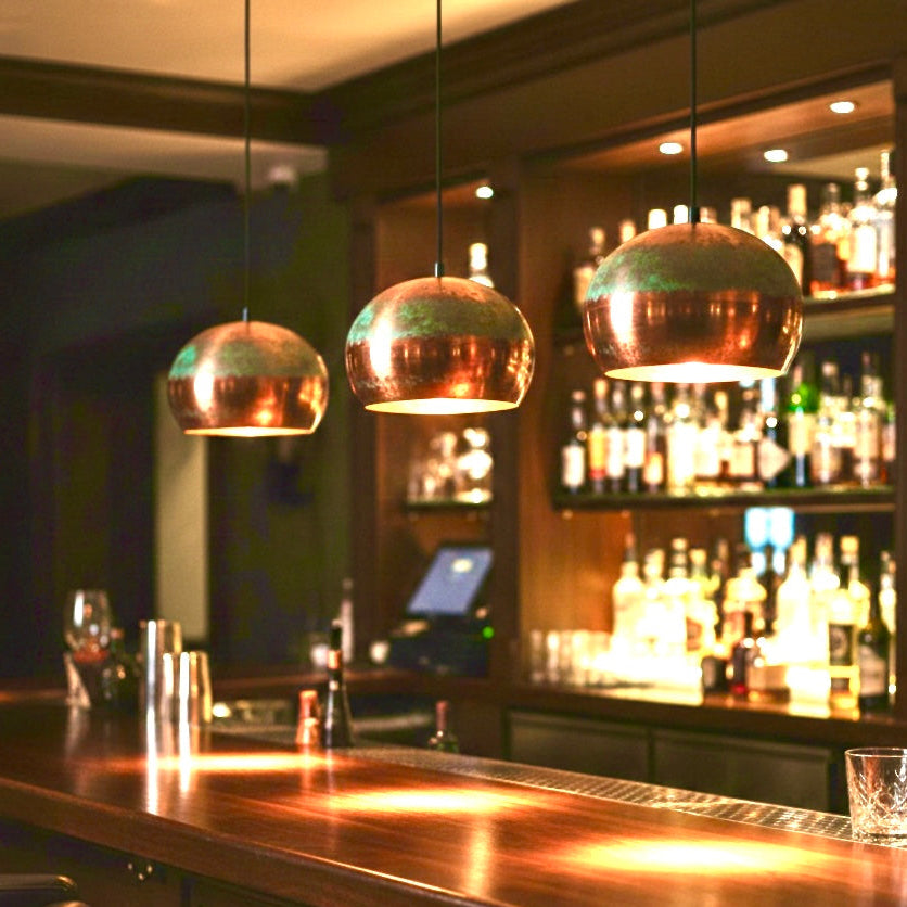 Copper and green patina pendant lighting over a high-end wooden bar, available for wholesale
