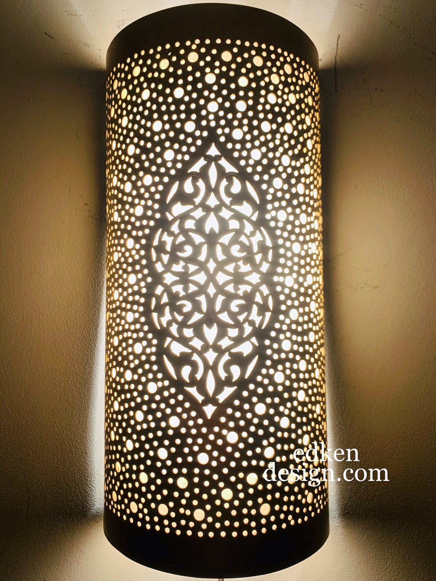 Illuminated Moroccan brass wall lamp casting a warm glow and intricate geometric shadows on the wall.